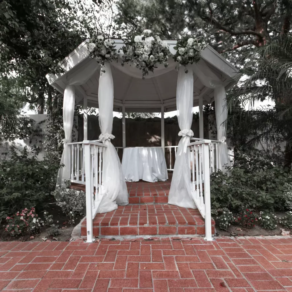 wedding decorated gazebo, image contains a gazebo with white curtains, and flowers on the entry of the gazebo